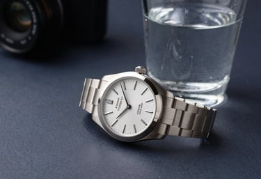 A sharp, high-contrast photograph of a silver luxury wristwatch next to a glass of water on a dark navy desk. This North American / US scene emphasizes professional punctuality and the intelligent, organized nature of our services.