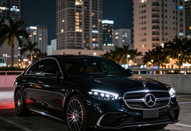 A sleek black luxury sedan parked in front of a modern Miami high-rise at sunset.