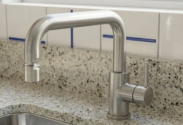 Modern brushed nickel kitchen faucet mounted on a granite countertop with white tiled backsplash.