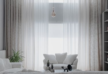 Modern living room with high ceilings, tall sheer curtains, and white corduroy sofas.