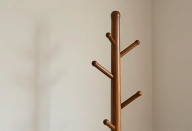 A close-up of a beautifully finished wooden coat rack (Mancebo) standing in a cozy corner. The wood has a rich #9E3A3A polish and the lighting is soft and inviting.