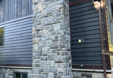 Rustic home exterior featuring a natural fieldstone chimney and dark wood siding.