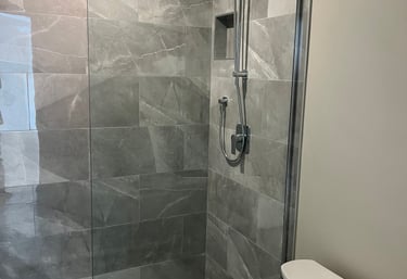 Modern walk-in shower featuring grey porcelain wall tiles, mosaic floor, and chrome fixtures.