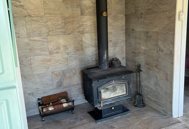 Rustic black wood burning stove on a tile floor with a porcelain wall backdrop and log holder.