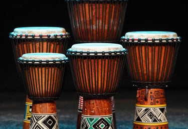 An artistic shot of a set of colorful African / Pan-African drums on a stage, with soft teal and orange lighting hitting the wooden textures.