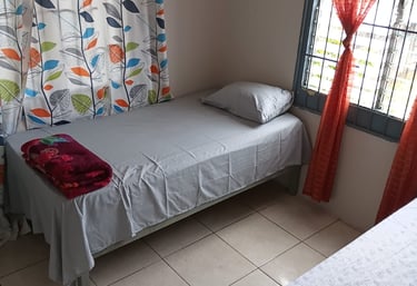 A tidy bedroom featuring a twin bed with grey sheets and colorful leaf-patterned curtains.