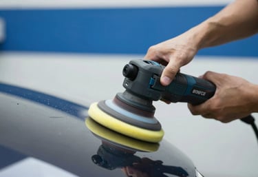 A focused shot of a professional detailer's hands using a dual-action polisher on a dark fender. The foam pad is spinning, and a small amount of polishing compound is visible. The background is a clean shop with #001220 and #E8F1F2 colors. Professional motion blur on the tool.