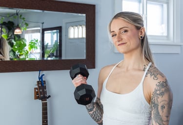 Jess Bartlett smiling warmly into the camera standing in a living room with a dumbbell