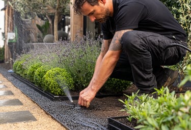 Professional landscaper installing a garden drip irrigation system with micro-sprinklers in a backyard.
