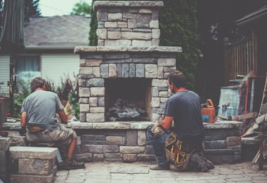 Two professional masons building a custom outdoor stone fireplace on a residential patio.