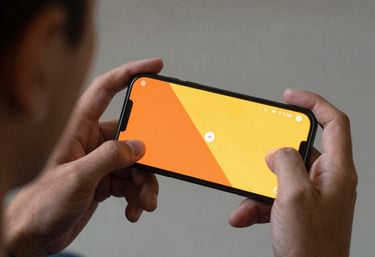 A professional photograph of a person testing a mobile game on their phone, seen from behind their shoulder. The screen is vibrant with orange and yellow colors.