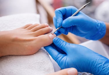 Professional nail technician in blue gloves performing a medical pedicure on a client's toenails