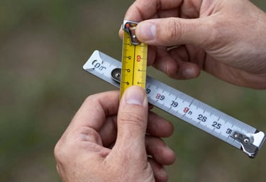 A smiling person checking their measurements using a mirror and a tape measure.