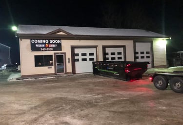 Pushaw Energy building at night with a large black dumpster parked in front of three white garage doors.