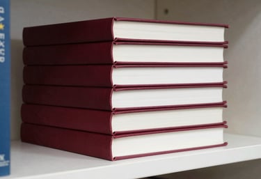 A close-up photograph of a stack of books with deep ripe crimson spines sitting on a clean, crisp parchment bookshelf.