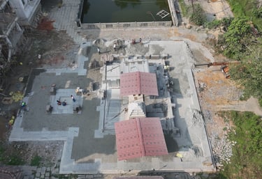Aerial view of a traditional Hindu temple under construction with red roof panels and stone masonry.