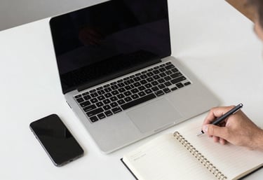 A top-down view of a professional workstation with a laptop, smartphone, and notebook in a bright, modern Brazilian office setting.