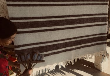 Una mujer cepilla una alfombra de lana a rayas tejida a mano que cuelga en un taller rústico tradici