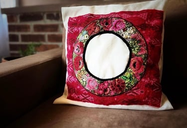 Cojín decorativo bordado a mano de origen guatemalteco con diseño floral sobre un sofá color café.