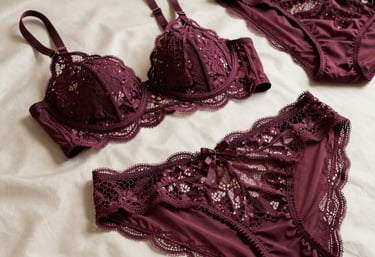 Editorial photography of a luxury lace lingerie set in deep plum color, arranged elegantly on a warm off-white silk surface. Soft side lighting highlights the texture and craftsmanship, suitable for a high-end European brand catalog.