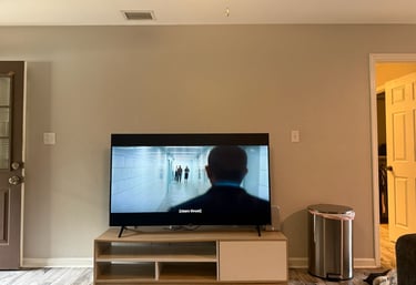 Modern flat screen TV on a wood entertainment center in a living room with beige walls.