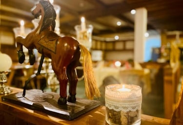 Wooden rearing horse statue next to a lit candle in a cozy, rustic restaurant setting.