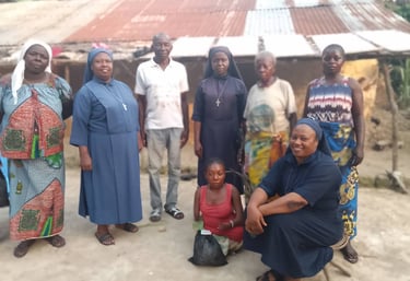 Catholic nuns in habits pose with a local community group in front of a village house for a mission project.