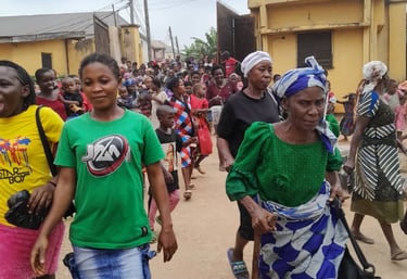A large crowd of people walking down a street in a Nigerian community for a local gathering.