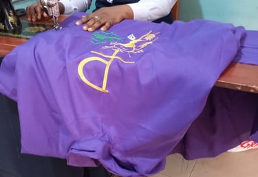 Tailor using a vintage sewing machine to embroider a gold religious symbol on purple liturgical fabric.