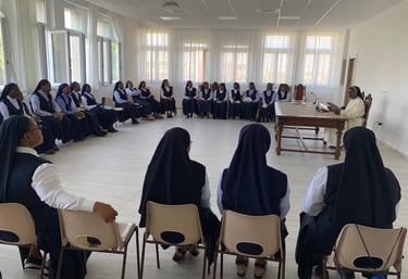 A large group of Catholic nuns in blue and white habits sitting in a circle for a meeting.