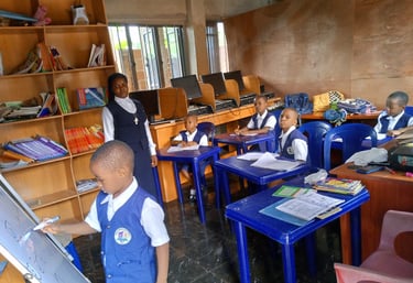 Students in blue school uniforms learn in a classroom with a teacher and computer workstations.