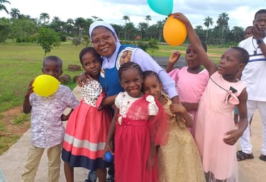 Smiling African children and a nun holding colorful balloons at a community celebration outdoors.