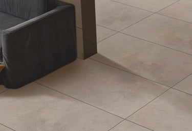 Manrise Enterprises- Modern interior with large beige tile flooring and a dark grey sofa.