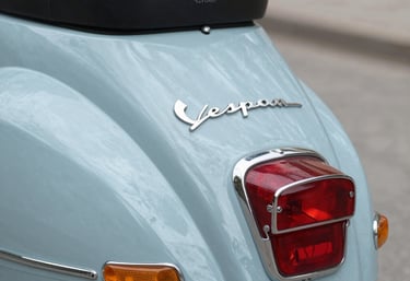 Classic electric Vespa parked on a cobblestone street with urban buildings in the background.