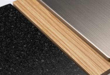 A macro photography shot of interior design samples: black granite, light oak wood, and brushed steel. Organized and clean, North American studio aesthetic.