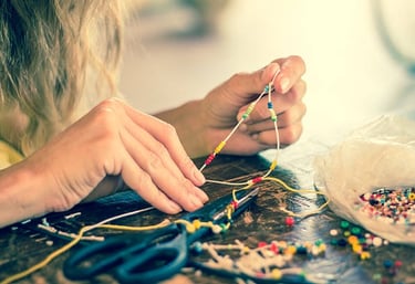 Close-up of hands crafting a handmade beaded necklace with colorful seed beads on a wooden table.