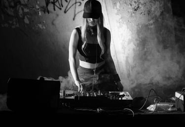 Kat Bendis wearing a cap mixes music on a pioneer rx3 in a smoky, underground club setting.