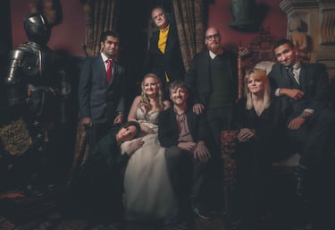 A diverse group in formal attire posing in a gothic room with a medieval knight suit of armor.