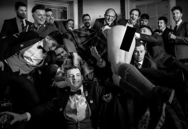 A group of men in formal suits and kilts celebrate in a black and white group photo.