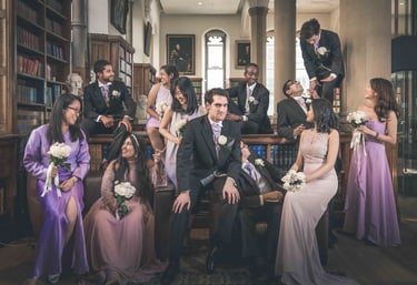 Diverse wedding party in formal suits and lilac dresses posing in a grand vintage library.
