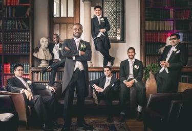 Groom and groomsmen in formal morning suits posing in a classic library for a wedding photo.