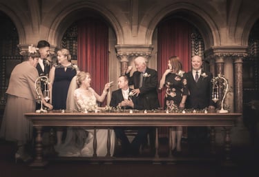 A joyful wedding couple and family posing at a vintage registry office signing table.