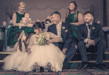 A formal wedding portrait of a bride, groom, and family in coordinated emerald green and white attire.