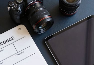 A top-down view of professional media tools: a high-end camera, a slate-colored script, and a tablet displaying a sleek digital interface. Arranged on a dark navy surface.