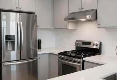 A clean, minimalist kitchen in a modern North American / US apartment featuring stainless steel appliances and white countertops.