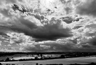 Black and white landscape of dramatic storm clouds over rolling rural farmland fields.
