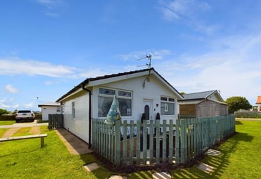 a small white bungalow chalet with a fenced in area