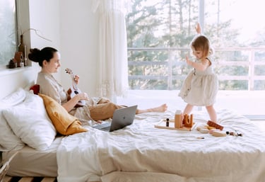 Light-filled bedroom featuring a mother playing a ukulele while her child joyfully dances nearby. Th