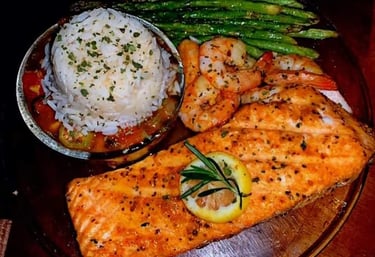 Grilled salmon fillet served with garlic shrimp, white rice, and roasted green asparagus on a plate.