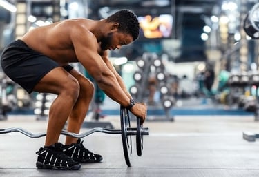 Shirtless athletic man preparing to lift an EZ curl barbell during a strength training workout in a gym.